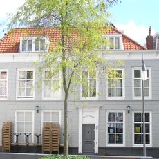 Breed hoekpand met gepleisterde rechte gevel aan de Vlasmarkt. Waarschijnlijk bestaande uit enige in de kern oudere panden, samengevoegd achter een 19e of begin 20e eeuw gevel in traditionele trant