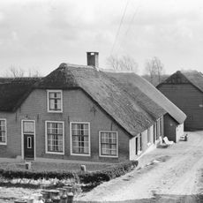Boerderij met puntgevel en links uitgebouwde opkamer. Vensters met goede roedenverdeling in de ramen. Houten schuur achter de boerderij