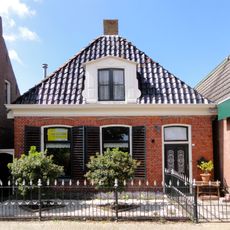 Pand zonder verdieping tegen gevels met houten gootlijst onder hoog schilddak met dakkapellen en topschoorstenen