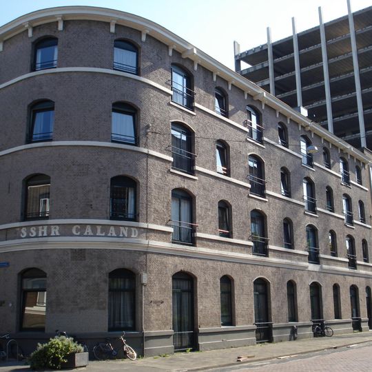 Bakstenen pakhuizen achter een doorlopende lijstgevel met hardstenen cordonbanden en getoogde vensters en deuren. Vormt een geheel met voorheen buurnummer Calandstraat 46