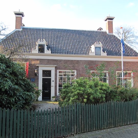 Lage langgerekte gevel met getande daklijst, houten deuromlijsting, schoorsteen op het dak