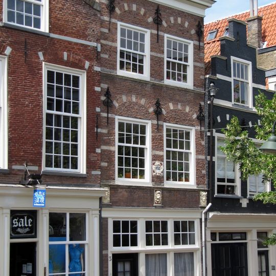 Pand met gevel, waarin geblokte ontlastingsbogen en sierankers, onder rechte lijst. Bij de restauratie werden een pui en een roedenverdeling in 18e-eeuwse stijl aangebracht.