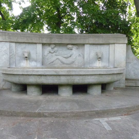 Monumentalbrunnen mit Steinrelief und Sitzbänken