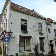 Brede gepleisterde gevel met rechte kroonlijst, ouder huis aanwezig