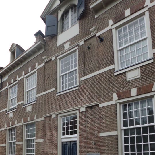 Royaal huis met verhoogde middenpartij door fronton gedekt. Hijsluik en balk. Natuurstenen blokken boven de ramen