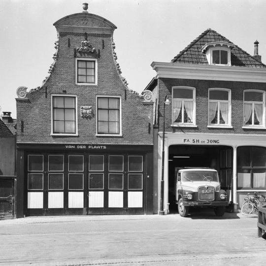 Pand onder zadeldak tegen klokgevel met gebeeldhouwde bekroning waarop siervaas