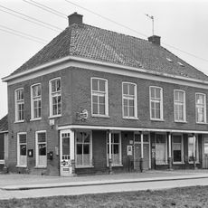 Vijf traveeën breed pand met verdieping die aan voorzijde rust op gietijzeren kolommen, zodat een veranda wordt gevormd (voorm. logement)