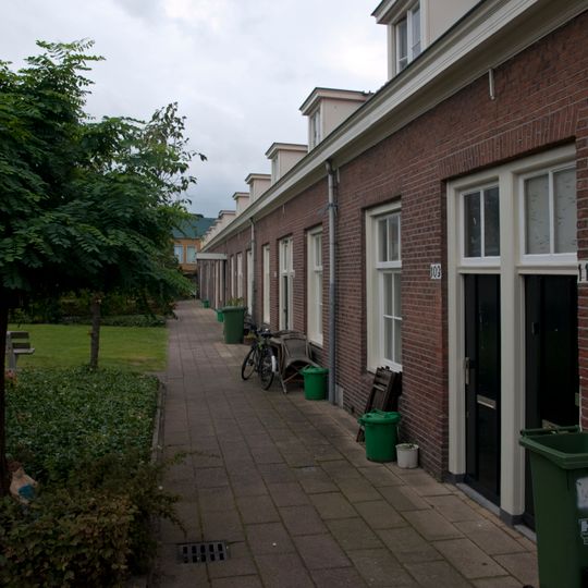 Gedeeltelijk dubbele- en gedeeltelijk enkele rij van in totaal achttien woningen op rechthoekige plattegrond, bestaande uit een bouwlaag onder een met pannen gedekt mansardedak