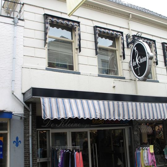 Pand onder dwars schilddak met gepleisterde lijstgevel en jongere winkelpui en met restanten van de middeleeuwse stadsmuur