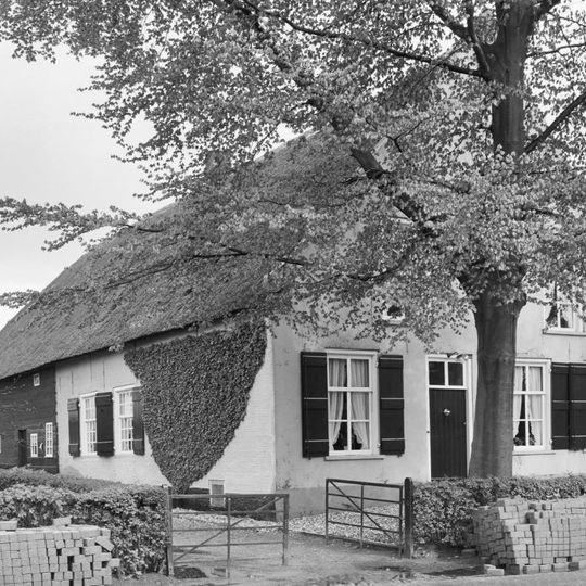Gepleisterde hoeve met puntgevel en rieten zadeldak. Stal van gepotdekselde houten delen achter het woonhuis onder hetzelfde dak. Vensters met zes- en 20-ruitsschuiframen en luiken.
