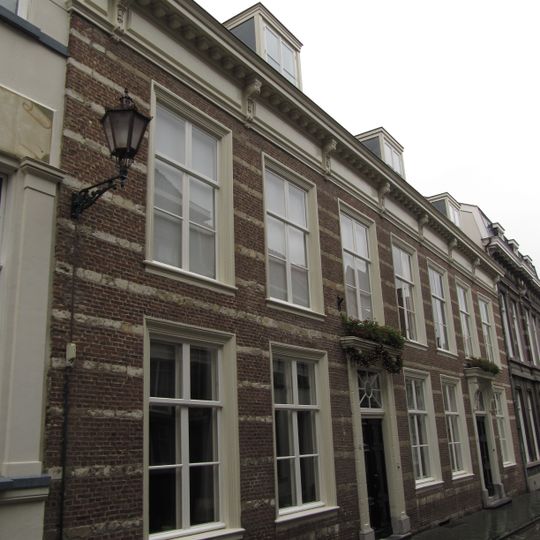 Huis met witgeschilderde lijstgevel waarin horizontale natuursteenbanden te onderscheiden zijn