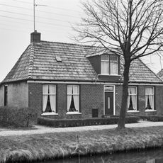 Landelijk pand met goot op klossen onder schilddak met hoekschoorstenen (vormt een geheel met nr. 26)