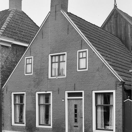 Pand tegen brede topgevel onder zadeldak met topschoorsteen