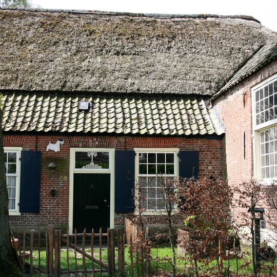 Boerderij op L-vormige plattegrond; het dwars naar de weg staande gedeelte met hoge kelder, topgevel met vlechtingen en duivengaten, ontlastingsbogen over de keldervensters.