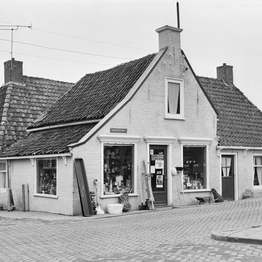 Eenvoudig pand met omgaande goot op klossen onder zadeldak tegen topgevel met twee aanbouwen