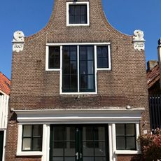 Pand onder zadeldak tegen klokgevel met aanzetkrullen en gezwenkte bekroning