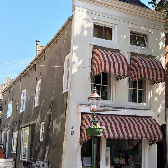 Diep hoekpand onder schilddak met gepleisterde voorgevel met rechte kroonlijst, waaronder lage zolderverdieping