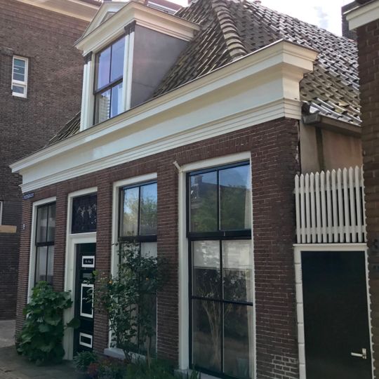 Laag hoekpand onder schilddak waarop middenschoorsteen met bord