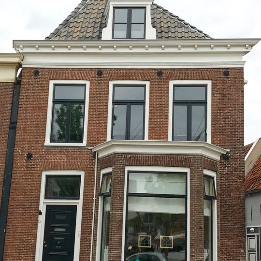 Hoekpand onder diep zadeldak tegen achtertopgevel en voorgevel met rechte kroonlijst, dakkapel en schoorsteen