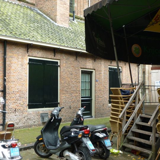 Laag pakhuisje gelegen tegen de noordoostzijde van de St.Joriskerk. Voormalige Diakoniewoning