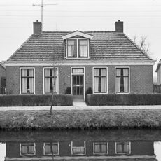 Dubbel landelijk pand met goot op klossen onder schilddak met dakkapel en twee hoekschoorstenen