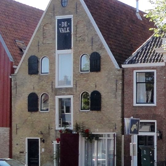 Pakhuis onder zadeldak tegen smalle topgevel met beitelingen en drie rechthoekige hijsluiken