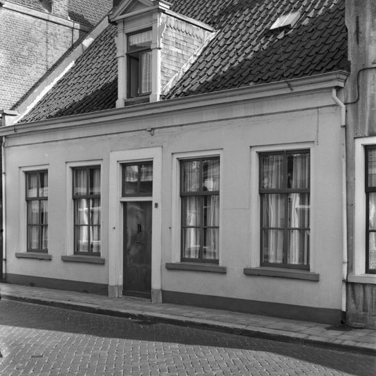 Eenvoudig dorpshuis met dwars zadeldak, twee haaks daarop staande achtergebouwen met topgevels en zadeldaken