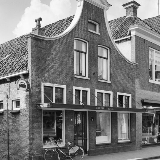 Pand onder zadeldak tegen driezijdig met hout bekroonde klokgevel