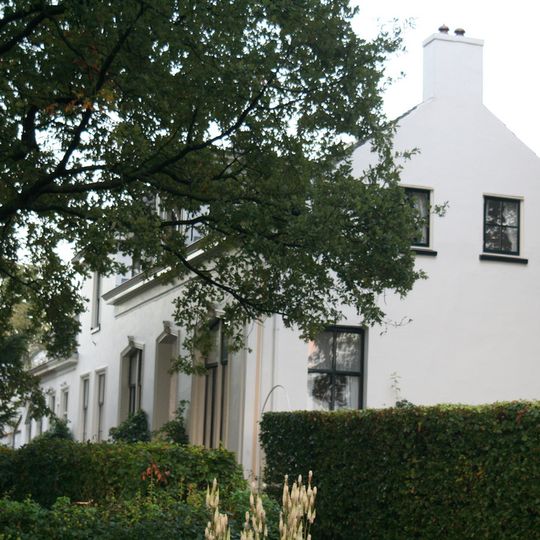 Complex van drie woningen, witgepleisterd. Linkergedeelte onder zadeldak, middengedeelte en rechtervleugel schilddak