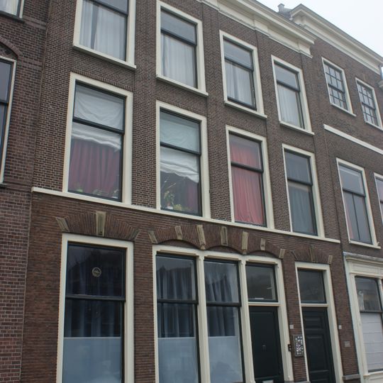 Pand met brede bakstenen gevel met pilasters en rechte kroonlijst. Onderpui verbouwd