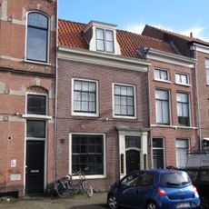 Pand met rechte kroonlijst, houten ingangsomlijsting met zijlichten en gebeeldhouwde deur