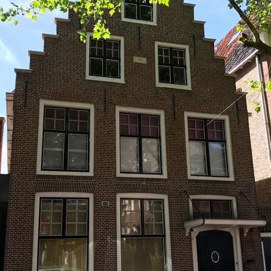 Hoog pand onder zadeldak tegen vernieuwde trapgevel met gevelsteen