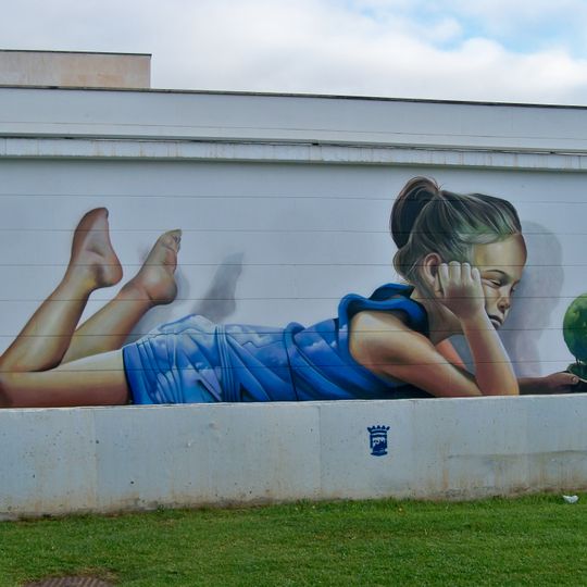 Mural de una niña vestida de azul tumbada bocabajo mientras sostiene con los ojos cerrados una maceta con una pequeña planta en forma de globo terráqueo.