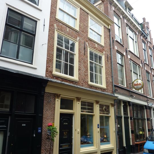 Pand met gepleisterde gevel onder rechte houten kroonlijst, met t-vensters en lage 6-ruitsschuifvensters meervoudige omlijstingen, in twee verdiepingen, afgedekt door zadeldak, evenwijd