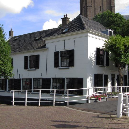 Hoekpand, rechthoekig woongedeelte onder dwars schilddak met gepleisterde lijstgevels en deuromlijsting door pilasters.