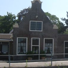 Ten dele houten huis met bakstenen puntgevel, voorzien van een halsje onder gebogen afdekking