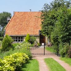 Daglonershuisje in baksteen met staafankers onder met pannen belegd schilddak met dakkapel, topschoorsteen en uileborden