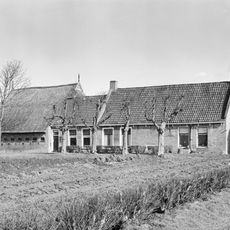 Kop-hals-rompboerderij met in het midden onderkelderd lang voorhuis onder zadeldak tussen topgevels waarvan de voorste vrijwel gesloten