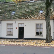 Wevershuisje bestaande uit begane-grond met pannen zadeldak, dat rechts aansluit tegen een puntgevel met rollaag en links doorloopt over nr 56. Gepleisterde voorgevel