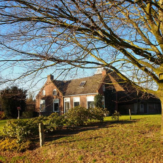 Keuterboerderijtje onder rieten dak tegen puntgevel met zesruitsvensters beneden en kleine lichtopeningen in de top