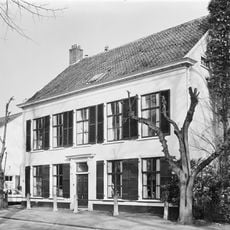 Huis met witgepleisterde lijstgevel, groene vensterluiken en ingang met kroonlijst op voluutvormige consoles