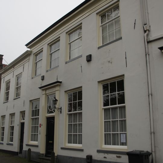 Huis met eenvoudige witgepleisterde lijstgevel met kleine roedenverdeling, in de vensters. 19e-eeuws karakter