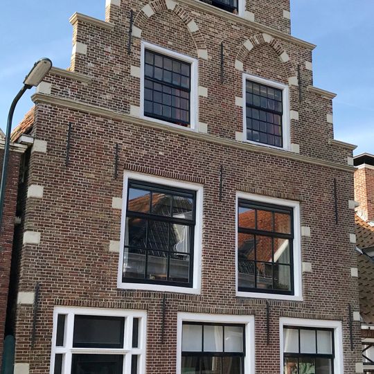 Pand met hoogoprijzende trapgevel versierd met hoek-, neg- en boogblokken rond de verdiepte vensternissen