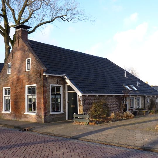 Woning met zesruitsvensters en kleine topvensters onder breed zadeldak met topschoorsteen met bord en stal in het verlengde van de woning