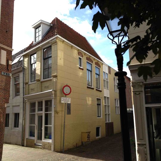 Hoekpand met geheel gepleisterde gevel met hoge beganegrond waarboven verdieping met pilasters in de vensterdammen