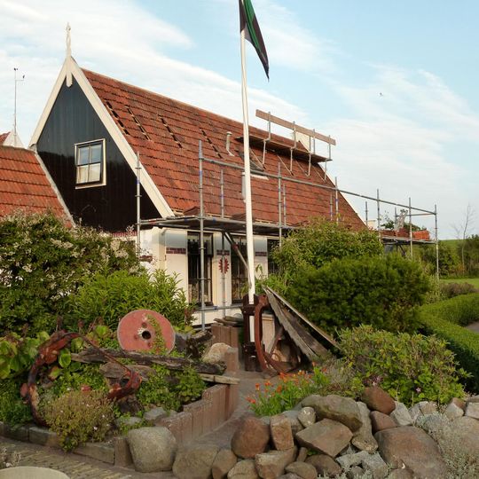 Hoekpand aan voorzijde van de gedempte havenkom met goed gedetailleerd houten voorschot. Bij dit pand behoort houten schuur met tuinpoortje erachter