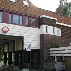 Poortgebouw met twee winkels met bovenwoningen, met veel hout zoals de zware kolommen in poort, bouwstijl Amsterdamse School, ligging aan Purmerweg centraal deel van Tuindorp Nieuwendam