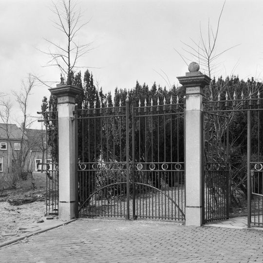 Naast de kerk het toegangshek tot het kerkhof met twee hardstenen hekpijlers,