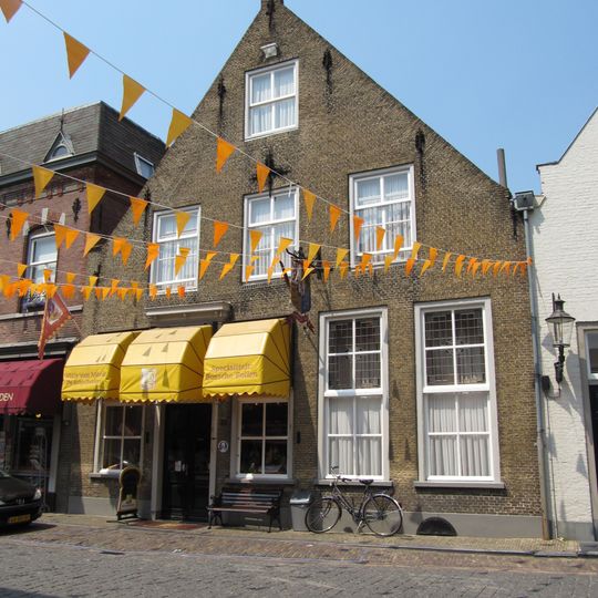 Huis met fraaie tuitgevel van gele baksteen met vlechtingen, gebeeldhouwde kraagsteen onder de top, sierankers en empire-ingang