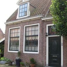 L-vormig huis, in hoofdzaak. Twee ingangen met vroeg 19e-eeuwse deur en snijraam. Drie dakkapellen met gebogen doorbroken frontons. Inwendig vier gesneden laatgotische sleutelstukken